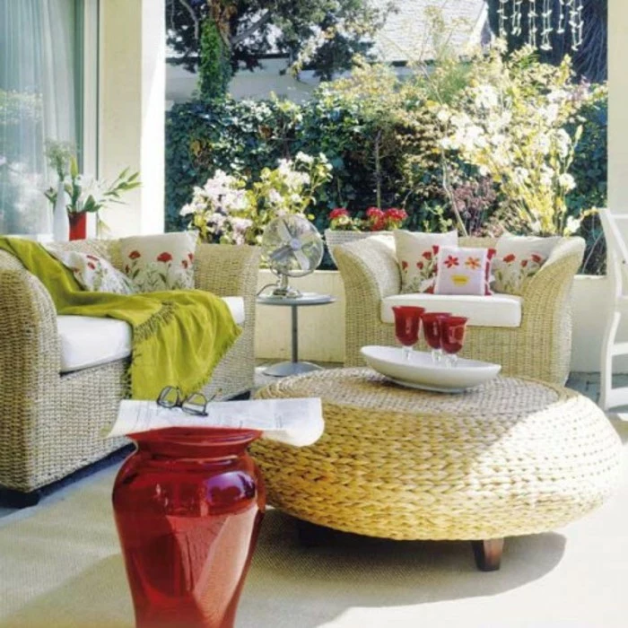 wicker furniture in a set, featuring couch and cozy chair, and a round table, front porch décor, with pillows and blanket, big red vase and decorations