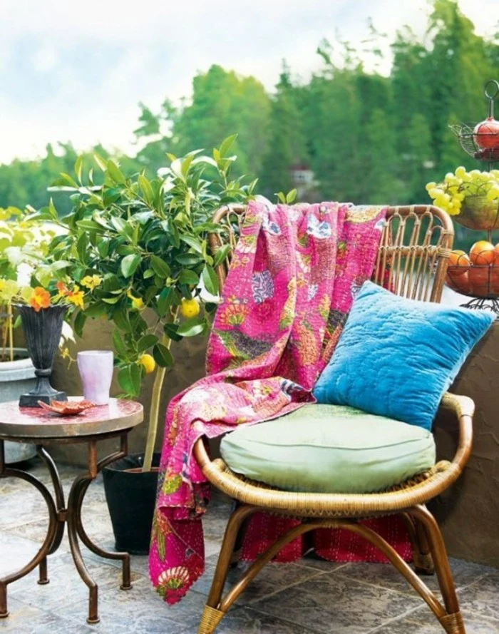 outdoor patio ideas, bamboo chair with green and blue pillows, and pink blanket with floral pattern, near small round table, and potted lemon tree with ripe fruit