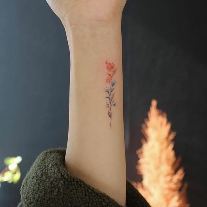 wildflower tattoo, close up of a stylized flower tattoo, in red and orange, blue and violet, on a person's upper arm