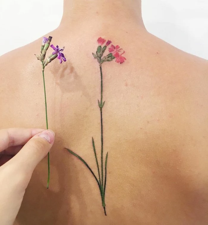 wildflower tattoo, close up of a bare female back, with a tattoo of a pink and green flower, a hand holding a very similar photo nearby