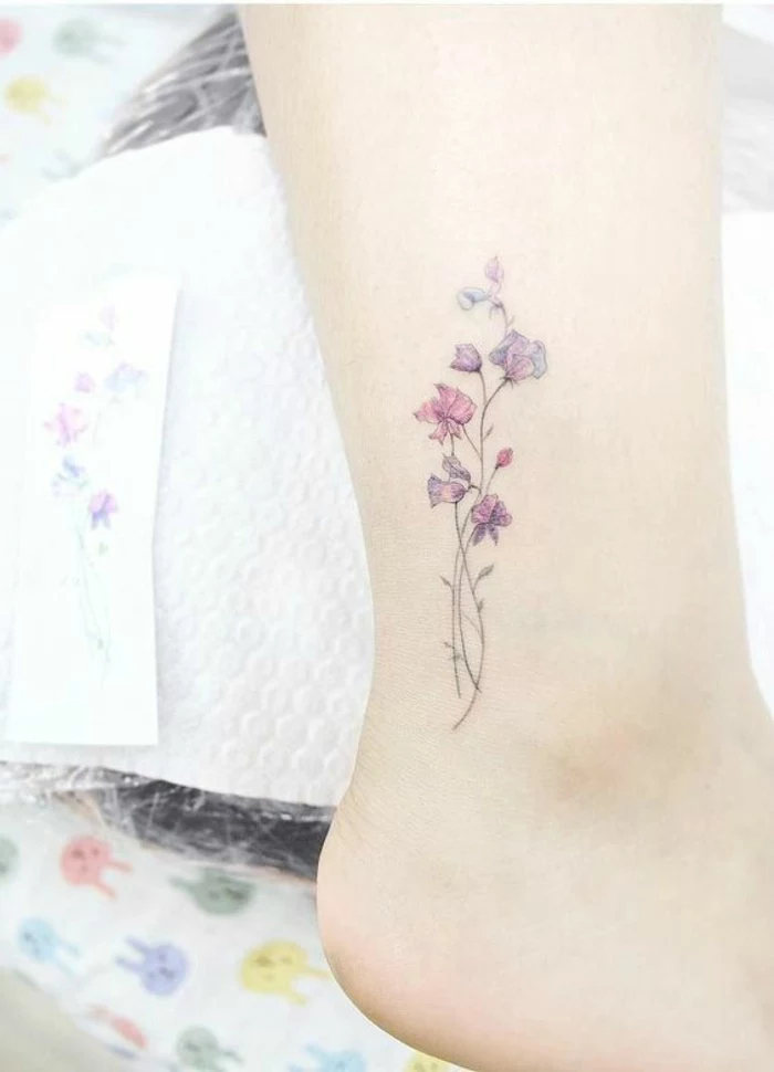 wildflower tattoo, three pale pink and purple flowers, with thin green stalks, tattooed on a person's ankle
