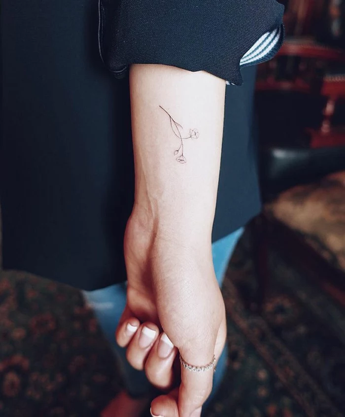 wildflower tattoo, female arm with french manicure and thumb ring, a tiny minimalistic tattoo of a flower, done in thin black ink, near her wrist