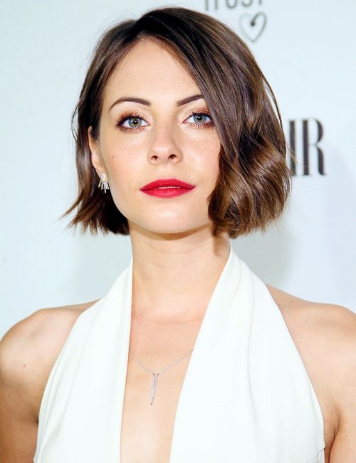smiling willa holland, wearing white halter neck top, and red lipstick, side parted wavy hair, short bob hairstyles