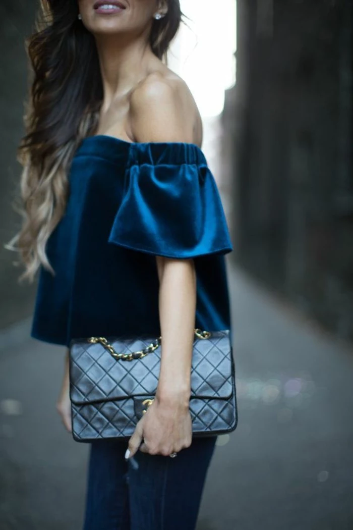 business casual women, dark blue velvet off-shoulder top, worn over dark jeans, by woman with wavy ombre blonde hair, holding black leather bag