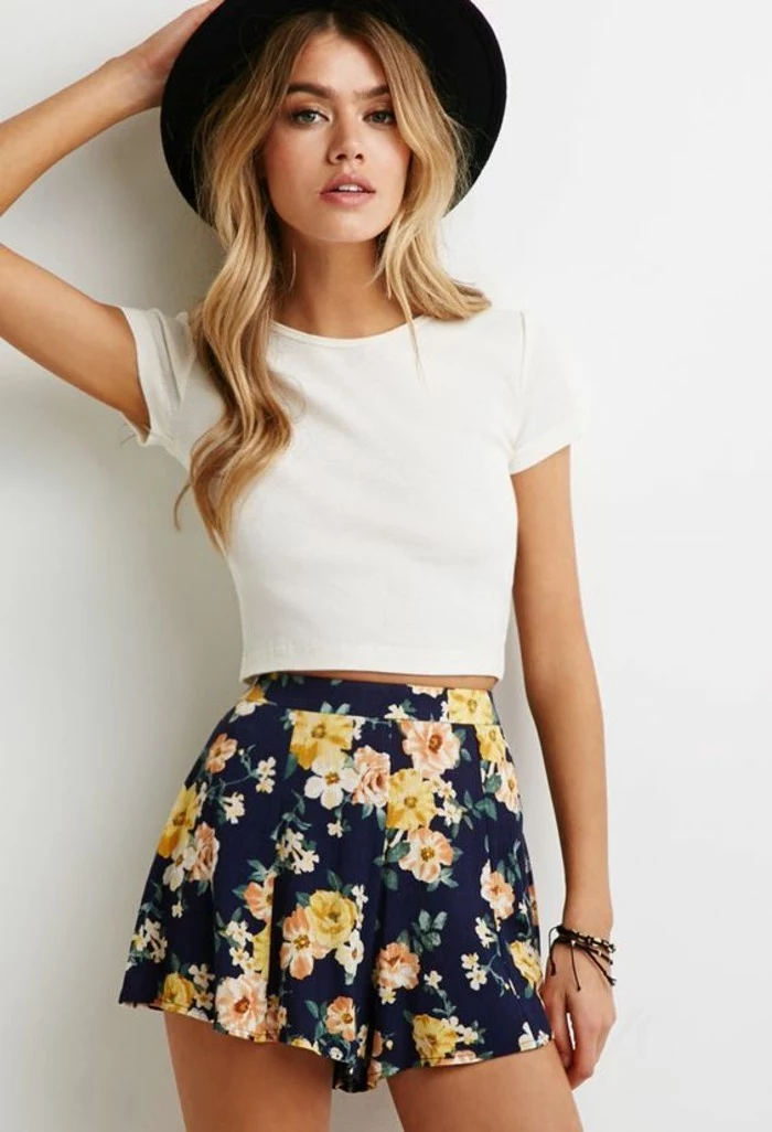 women outfits, plain white cropped t-shirt, and dark blue high-waisted shorts, with white, yellow and orange flowers, worn by blonde woman with long wavy hair, and black felt hat
