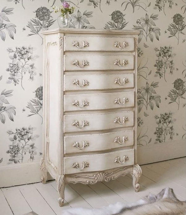 chest of drawers in antique style, painted in shabby cream color, country cottage furniture, on white floor, near goatskin rug, and floral wallpaper in white and grey