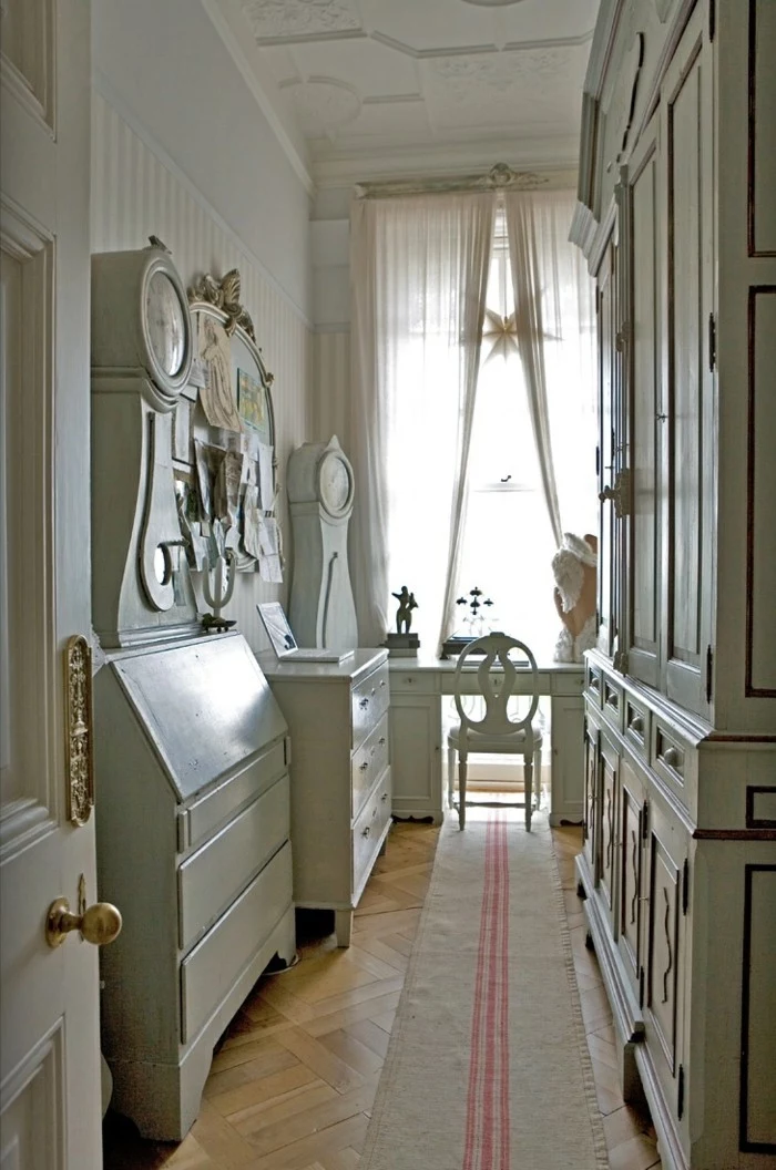 long hallway runners, pale wooden laminate floor, white antique furniture, including a wardrobe, several cupboards and a desk, with a matching chair, long beige rug, with three pink stripes