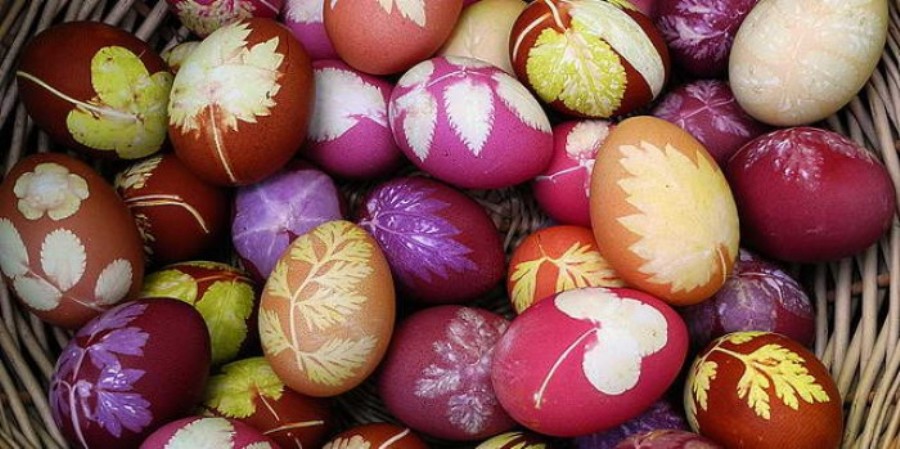 a variety of eggs, dyed in pink and red, orange and yellow, with different botanical shapes printed on them, in white yellow and green, easter egg coloring with with flowers