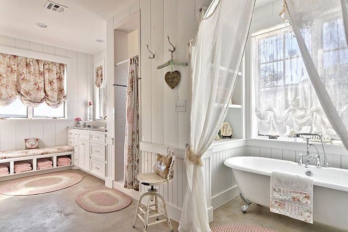 floral curtains in cream and pink, inside a bathroom with white wooden paneling, and smooth beige floor, white bathtub with silver ornamental legs, shabby chic decorating, sheer white curtains