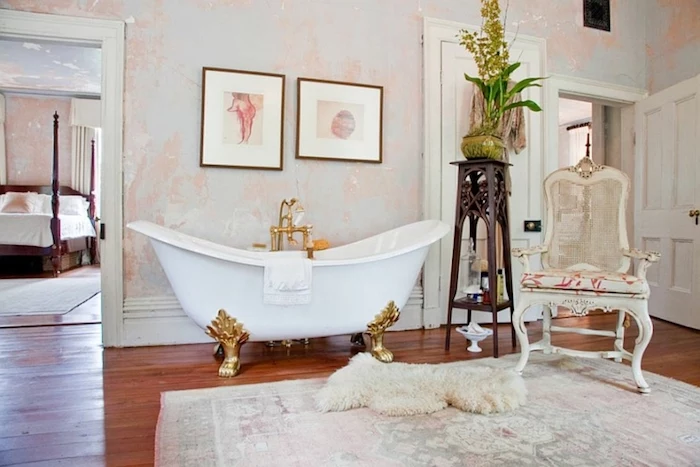 bathtub in white, with golden ornamental legs, shabby chic furniture, on wooden floor with faded rug, and fluffy lambskin throw, near antique chair and various decorations