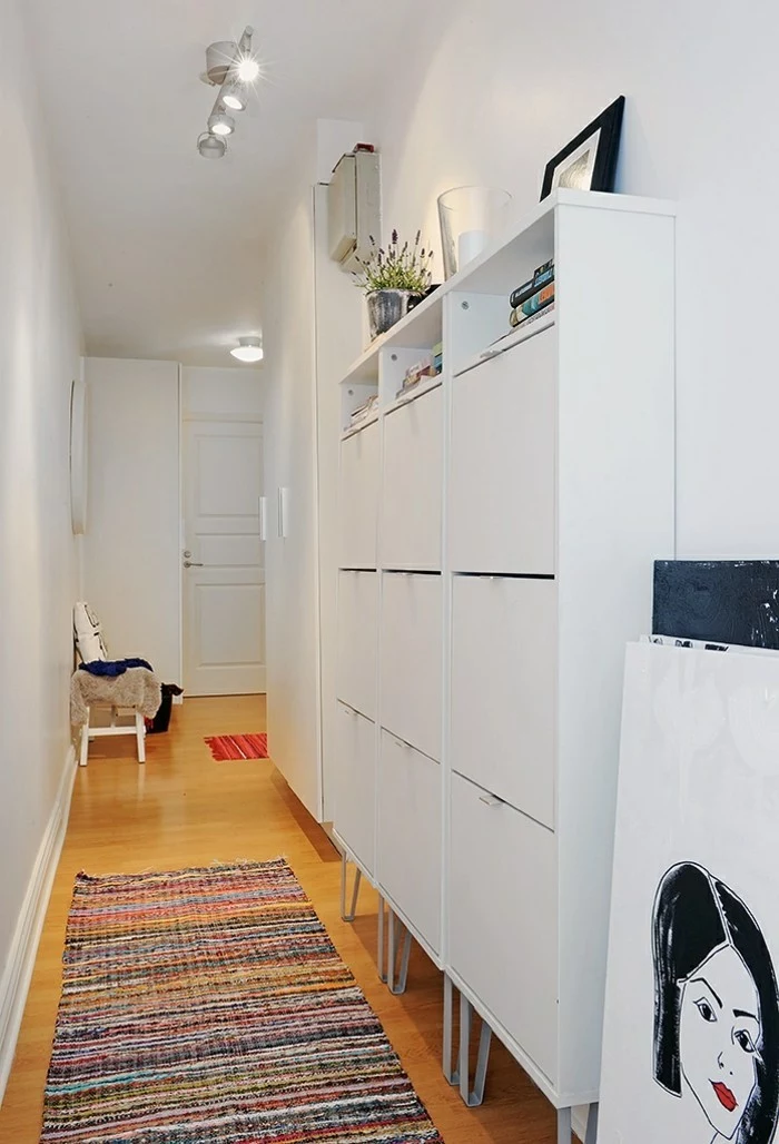 modern hallway with white walls, pale orange laminate floor, white cupboard and multicolored rug