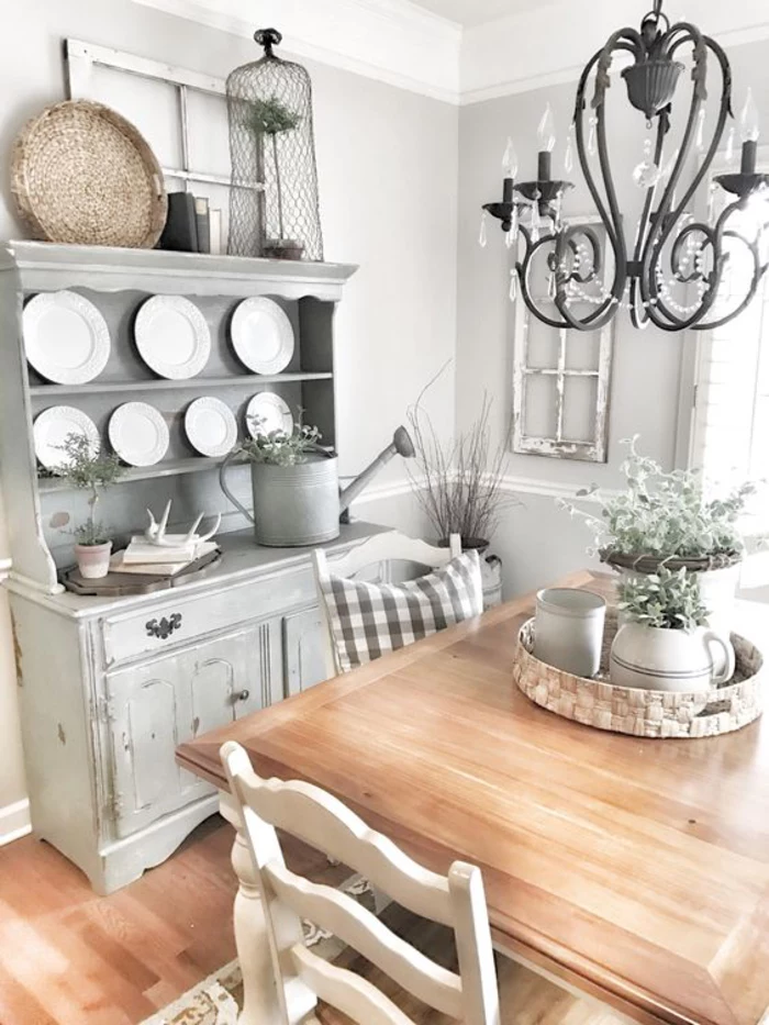 round white plates, on pastel grey dresser, vintage chic style, black wrought-iron chandelier, square wooden table with chairs