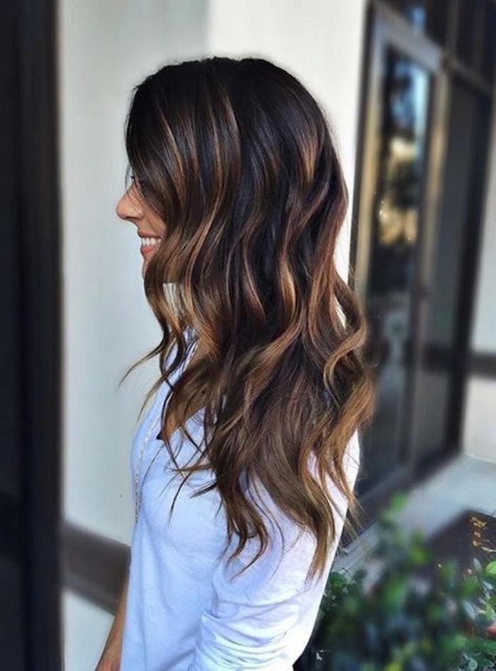 blonde balayage on curled brunette hair, dark brown hair colors, on smiling woman, in pale sweater, facing to the side