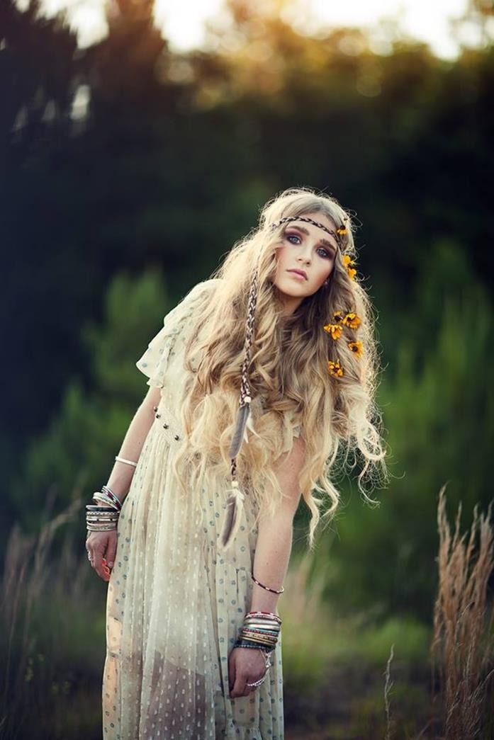 boho clothing, semi sheer white maxi dress, with polka dot pattern, and floaty short sleeves, worn by young woman, with long curly hair, decorated with small braid, flowers and feathers