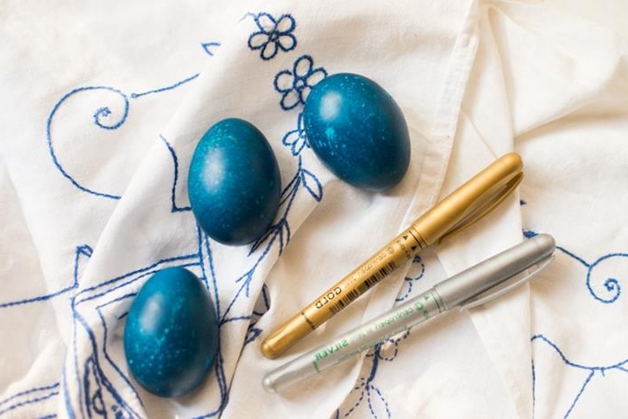 spotty blue eggs, placed on cream fabric, with blue floral embroidery, how to dye easter eggs, near a gold and a silver pen