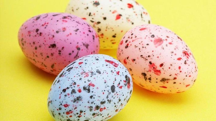 speckles in red and black, on easter eggs dyed in yellow, pink and blue, placed on a bright yellow surface