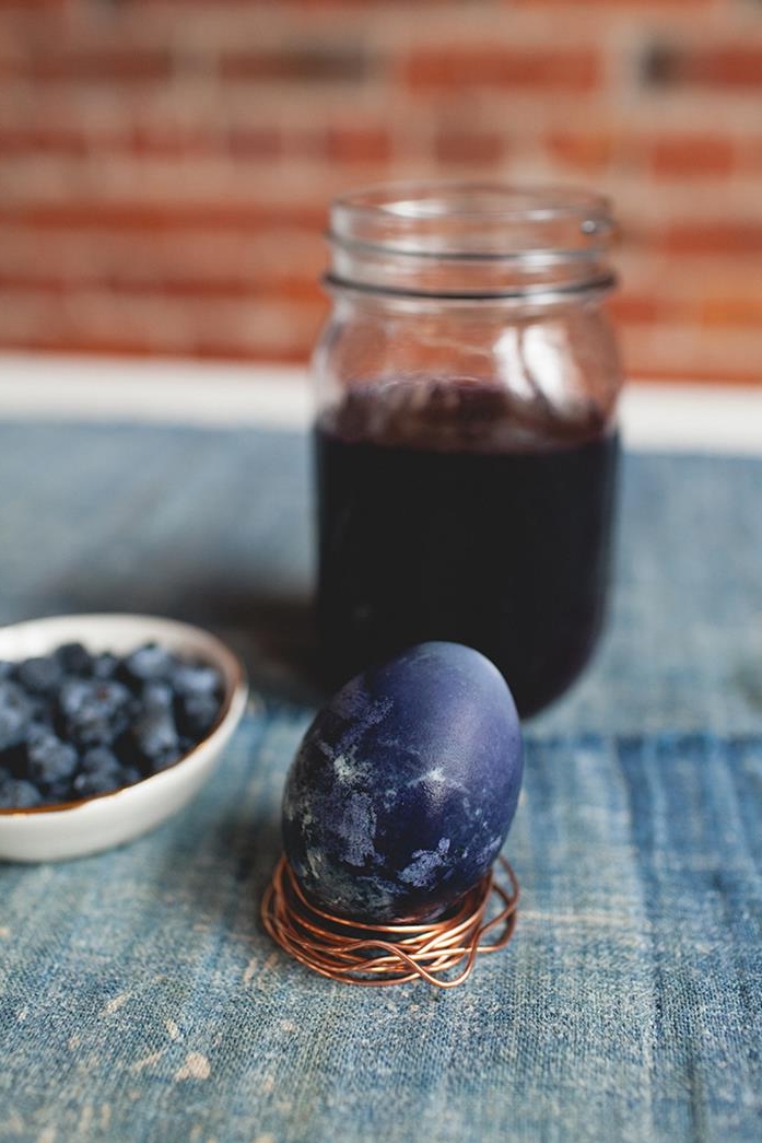 easter egg coloring, mason jar containing natural blueberry dye, near small plate with fresh blueberries, and an egg, dyed in spotty blue color