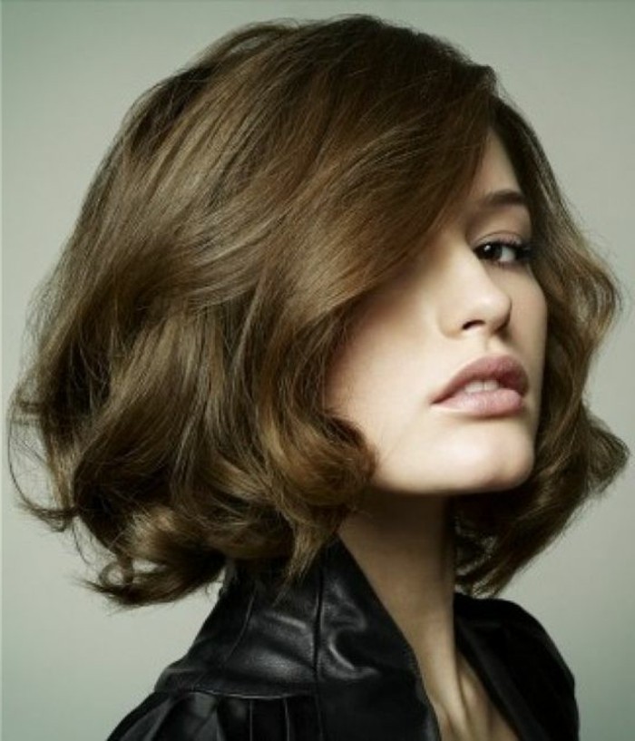 side-swept curled bob, in medium brown hair color, worn by woman in black leather top, with pale nude pink lipstick 