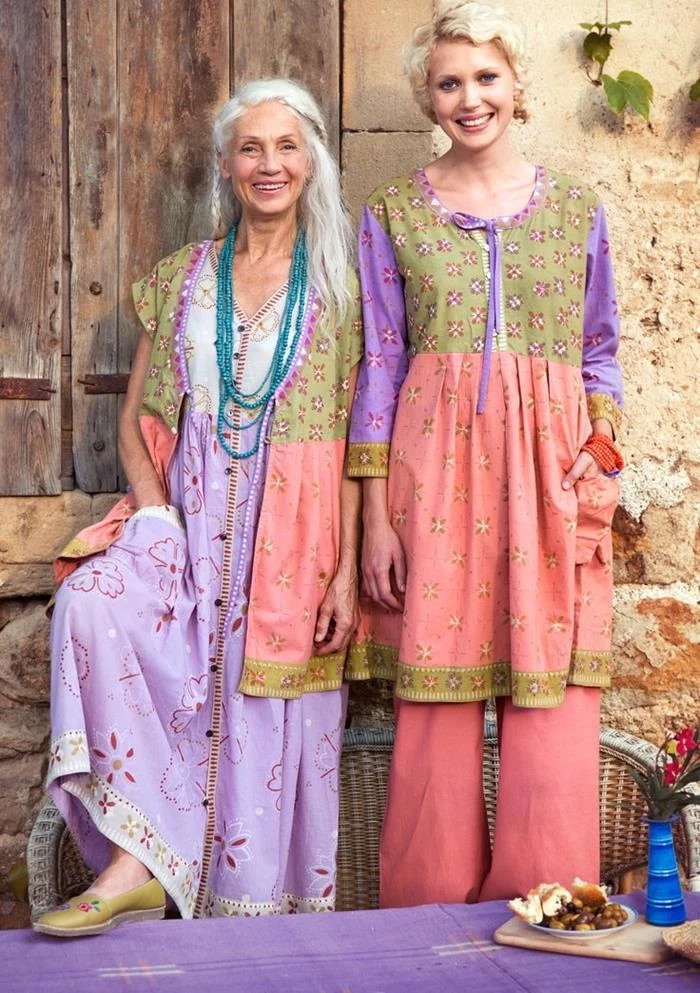 older woman with long white hair, standing next to young blonde woman, both wearing bohemian style outfits, in pale purple, pink and pastel green, with floral pattern and pockets