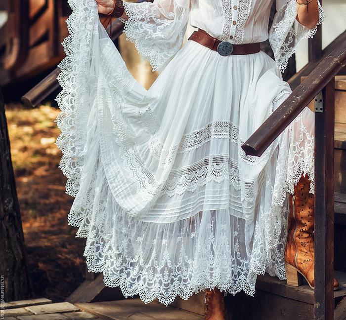 tiered white boho style dress, with lace and frills, worn with vintage brown leather belt, by woman standing on wooden stairs