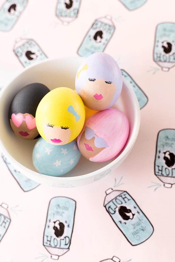 funny women's heads, with pink or yellow, grey or black hair, some with sunglasses, painted on eggs, placed in a white bowl, how to dye easter eggs