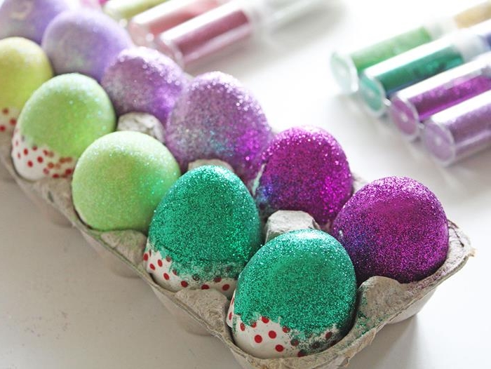 cardboard egg box, with several glitter-covered eggs inside, coloring easter eggs in light and dark purple and green, with washi tape across the middle