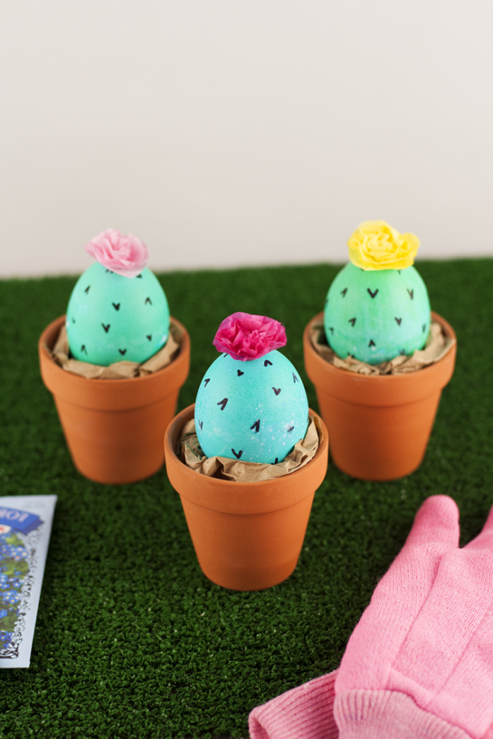 easter egg designs, three eggs painted green, and made to look like cacti, with black thorns drawn in marker, and faux flowers on top, placed in orange ceramic pots