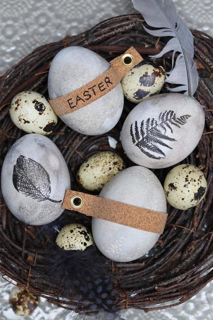 quail eggs placed inside a nest, made from brown twigs, near feathers and four hen's eggs, dyed in pale spotty grey, and decorated with leaf patterns and labels