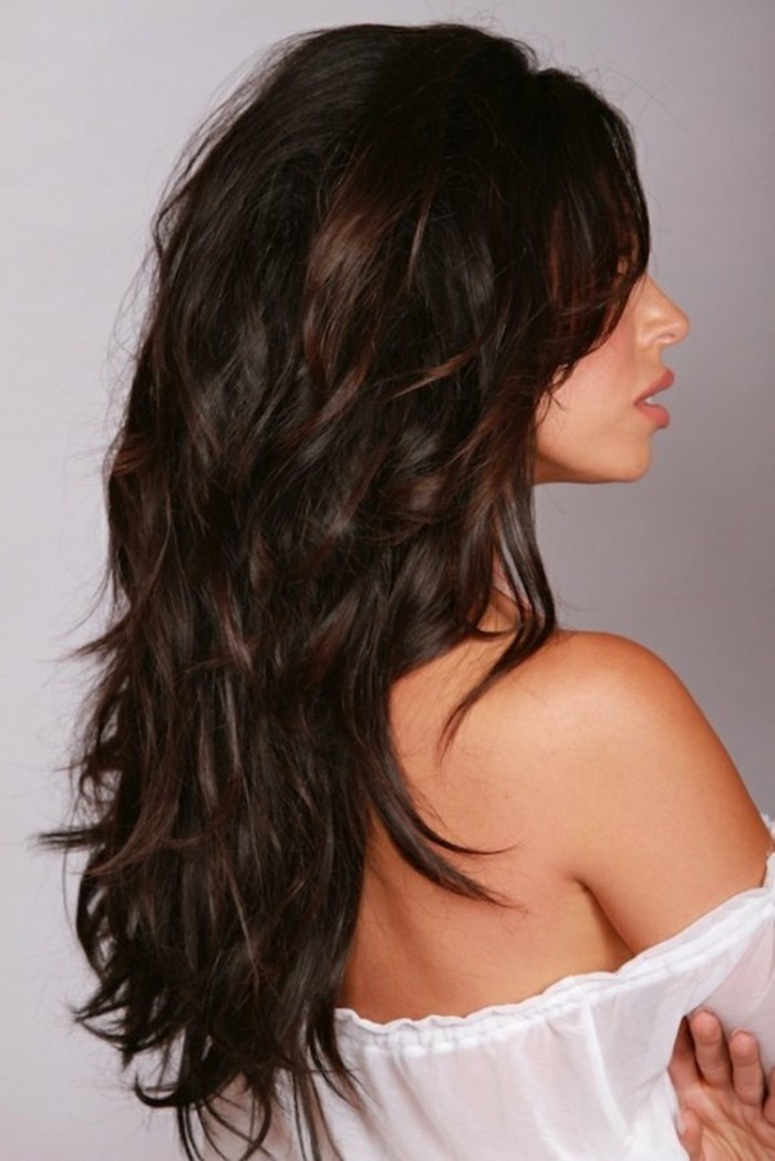 curled and long, dark reddish-brown layered hair, worn by woman looking to one side, in a white off-shoulder dress