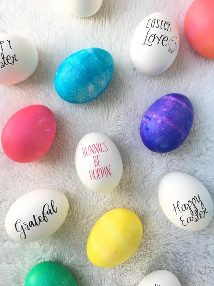 messages written in different fonts, in red and black, on white eggs, placed on white surface, near pink and blue, yellow green and purple dyed eggs, easter egg coloring variations 