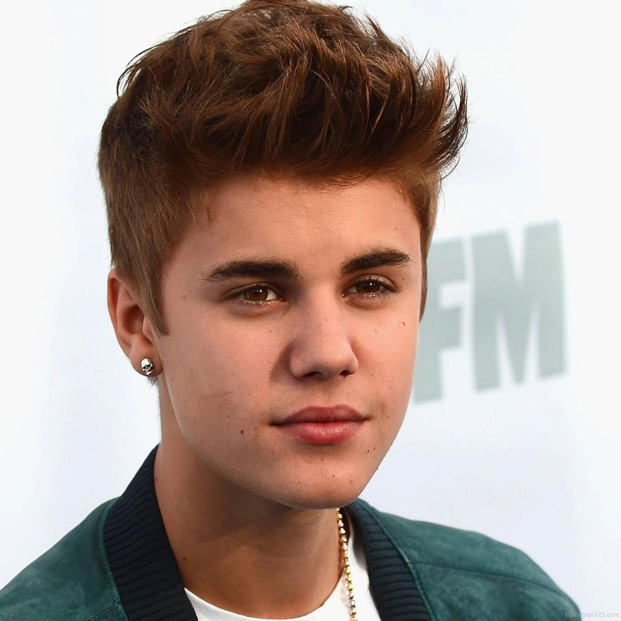 young justin bieber, with auburn hair, bangs styled in upward facing spikes, cool haircuts for boys, he is wearing white t-shirt and green jacket