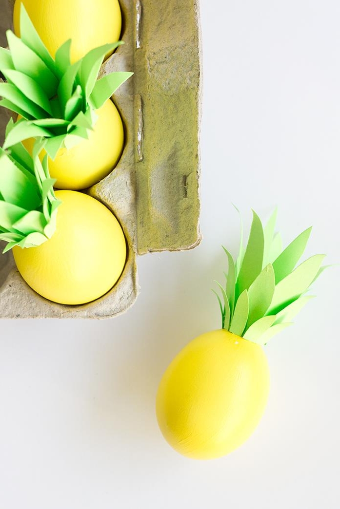 completed pineapple eggs, all died yellow, and decorated with pale green paper leaves, dying easter eggs, several inside a cardboard box, one laying outside of the box