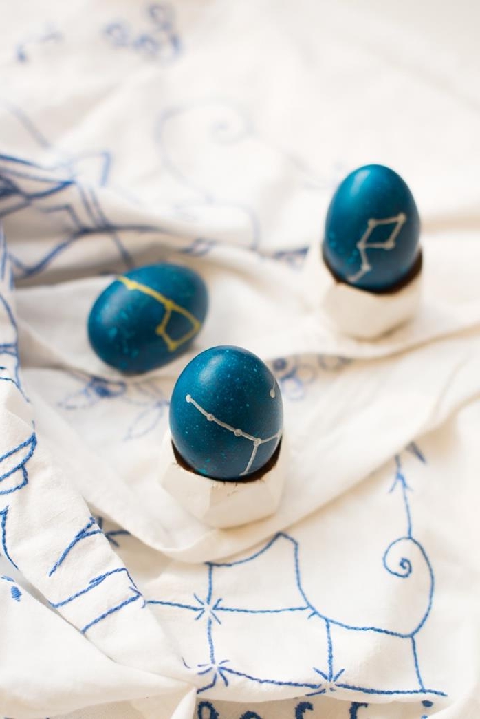 navy blue eggs, decorated with drawings of constellations, done in gold and silver marker, how to dye easter eggs, white fabric with blue embroidery in the background