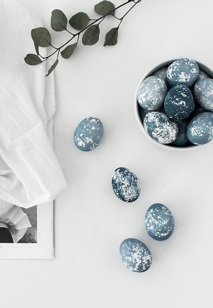 spotted dark blue dyed eggs, placed on white surface, near branch with green leaves, and a framed portrait, almost covered in white cloth