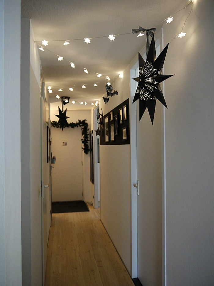 simple narrow corridor, with white walls and doors, decorated with lit star-shaped chain lights, black garlands, and large black star lanterns