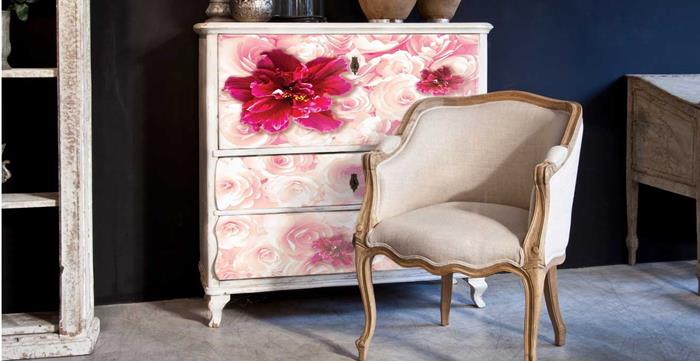 fuchsia and pale pink flowers, painted on white antique chest of drawers, near a pale beige armchair, with wooden legs and armrests