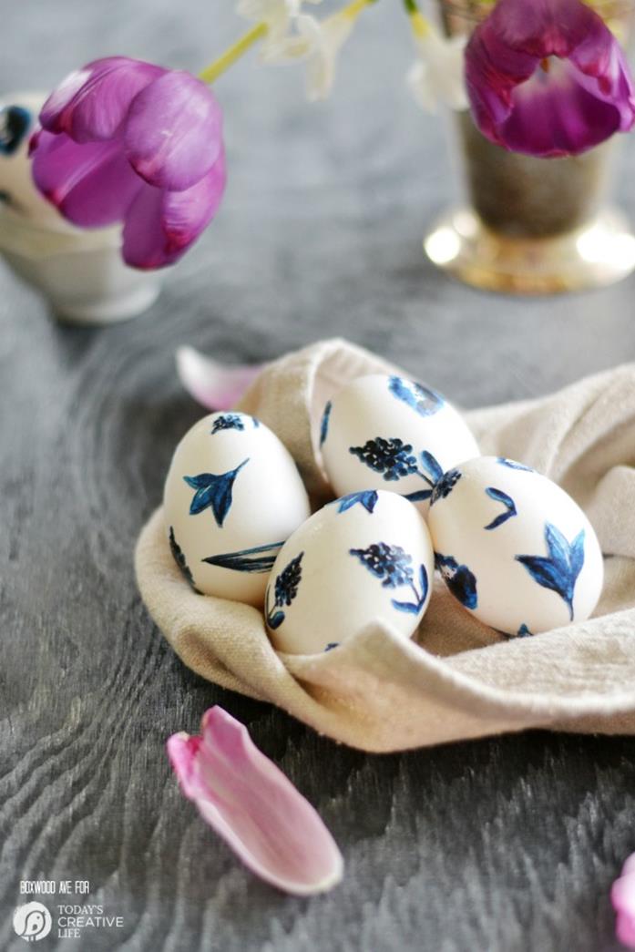 tulips in purple, near a cream-colored cloth, with four white easter eggs, decorated with hand-painted, dark blue flowers