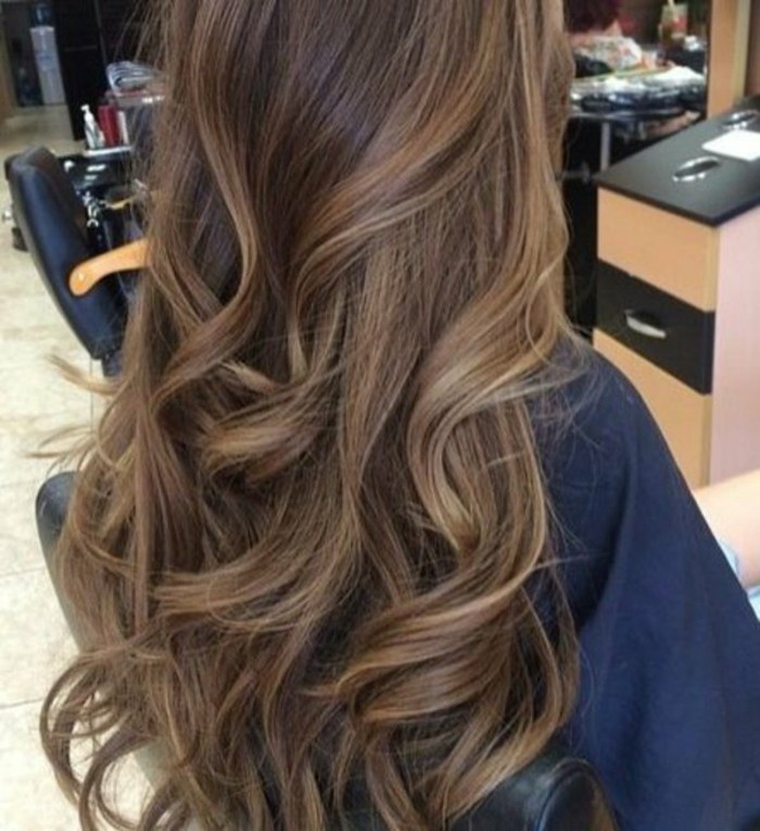 curled long brown hair, with discreet honey blonde highlights, brunette hairstyles, worn by woman, in navy robe, sitting on a hairdresser's chair