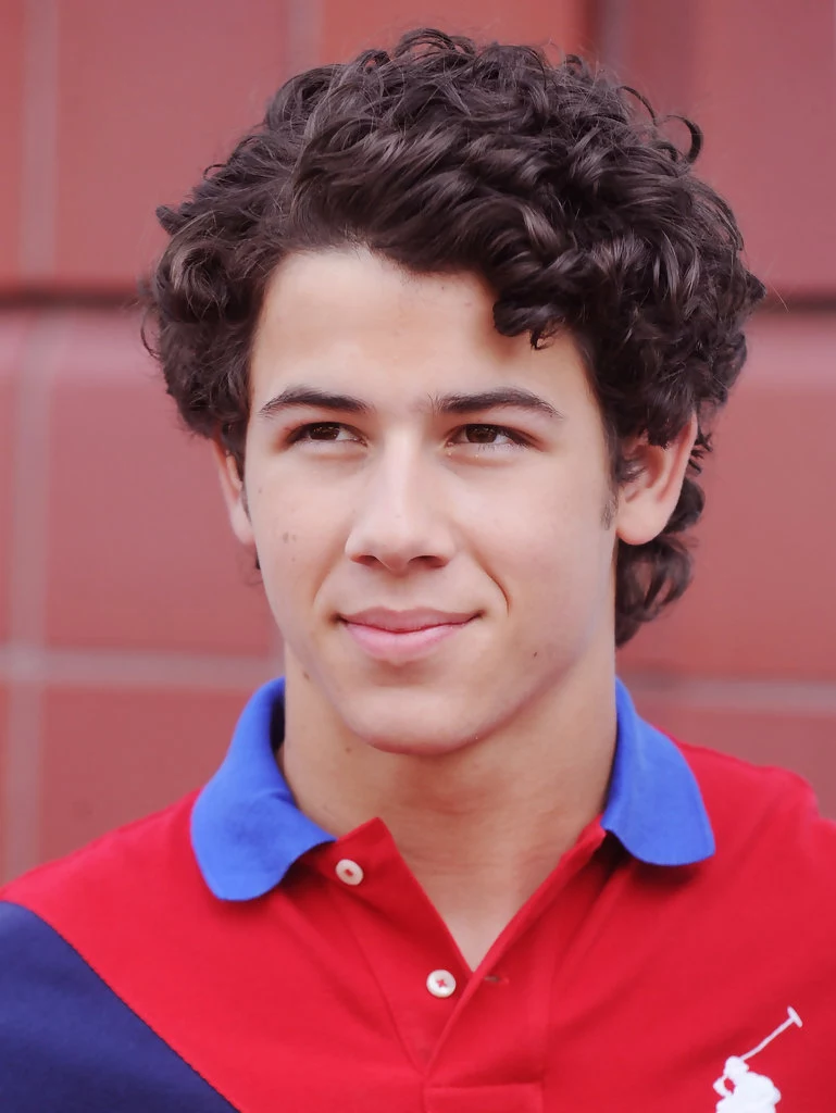 brunette man with dark, shiny and curly hair, with side part, hair designs for boys, he's wearing a red, blue and violet polo shirt 