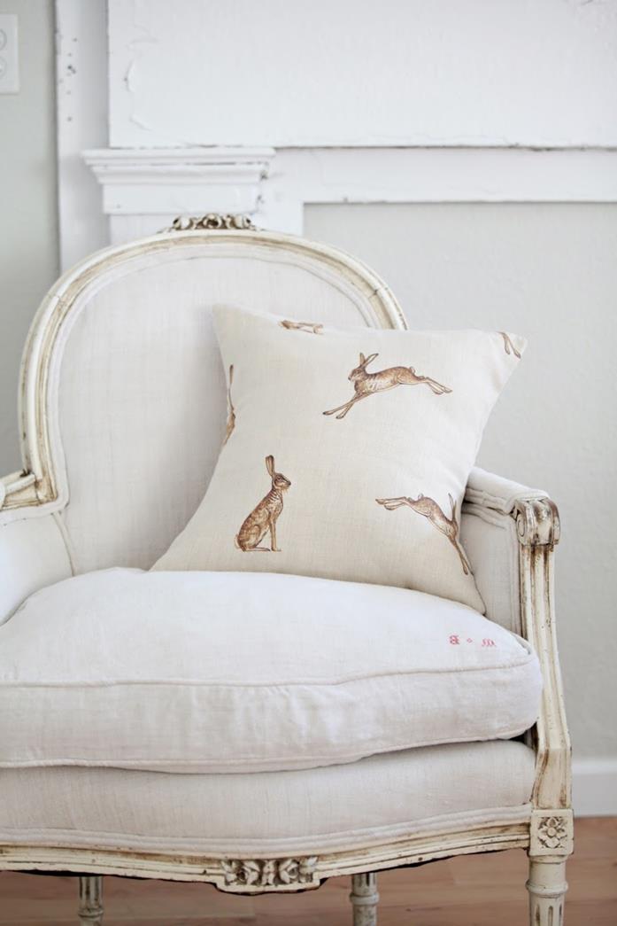hare print pale cream cushion, on off-white antique chair, with ivory-colored details, country cottage furniture, white background and wooden floor