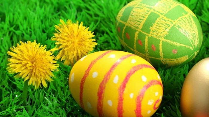 bright green egg, decorated with yellow and red crayon scribbles, near yellow egg, with red and white scribbles, forming a pattern, how to dye easter eggs, green grass and two yellow dandelions