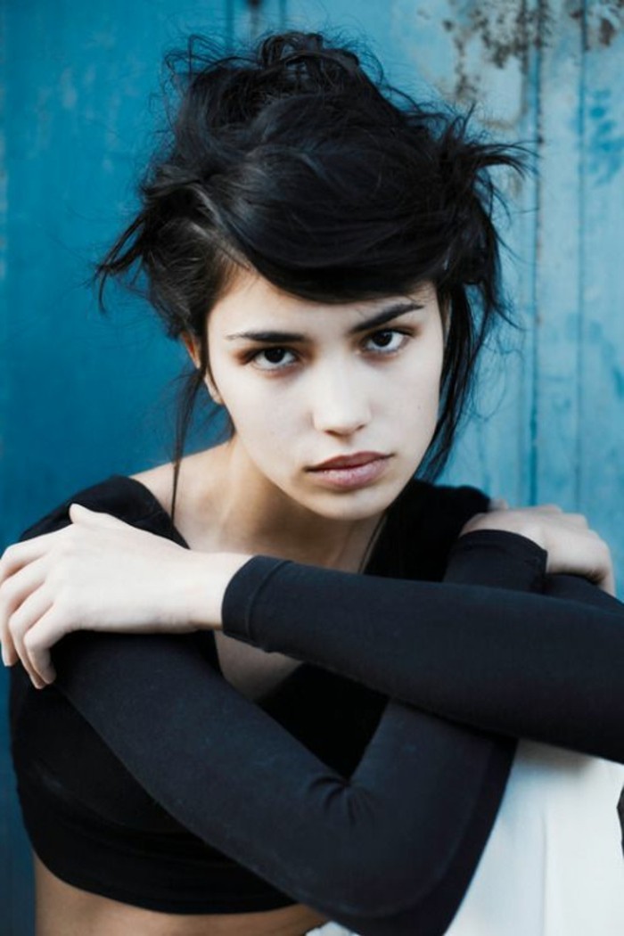 sloppy messy bun, with side bangs, rebellious punk-style, dark brown hair colors, worn by pale, black-eyed girl, wearing black cropped top, with long sleeves