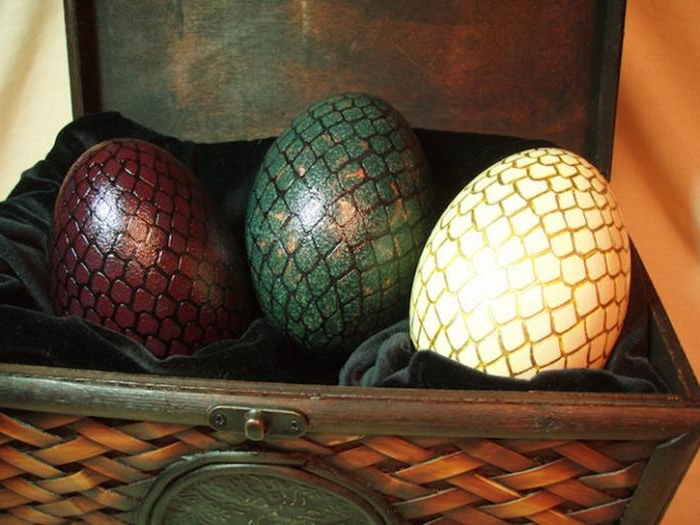 game of thrones inspired dragon easter eggs, ostrich eggs painted in yellow, green and dark red, with hand-drawn golden and black scales, placed inside a chest