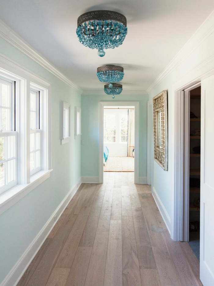 small hallway ideas, hall with pale duck's egg blue walls, windows with white windowpanes, mirror in ornate golden frame, three blue crystal chandeliers, pale wooden floor