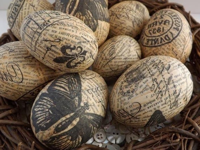 vintage newspaper decoupage easter eggs, decorated with black stamp-like patterns, butterflies and fancy writing, placed in a nest with many clothes buttons