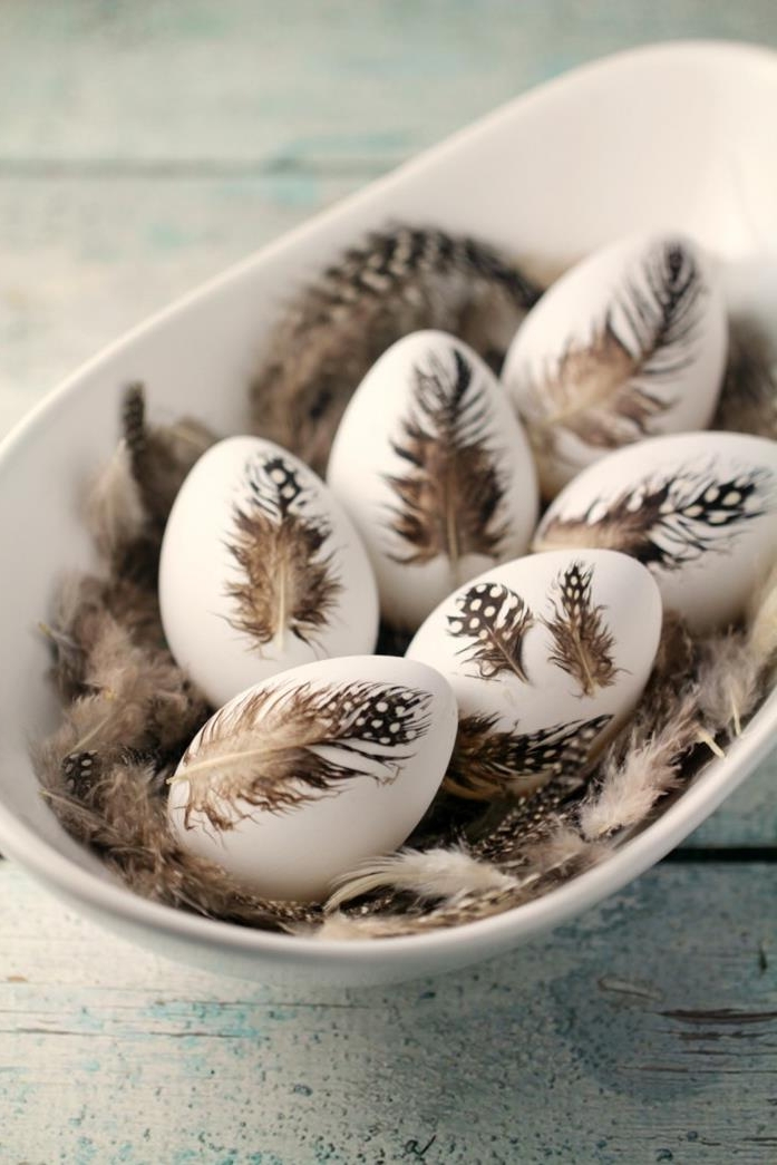 six white hens' eggs, decorated grayish-brown, white spotted quail feathers, easter egg decorating, inside a white oval dish, with more quail feathers