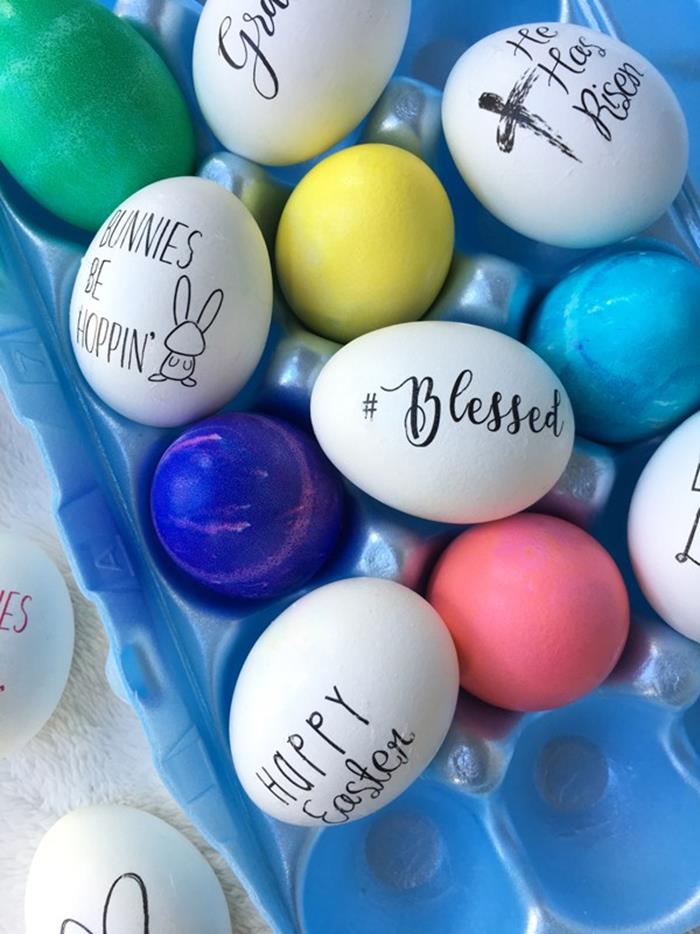 easter greetings written in black sharpie, on plain white eggs, placed near eggs dyed in green and blue, pink and yellow