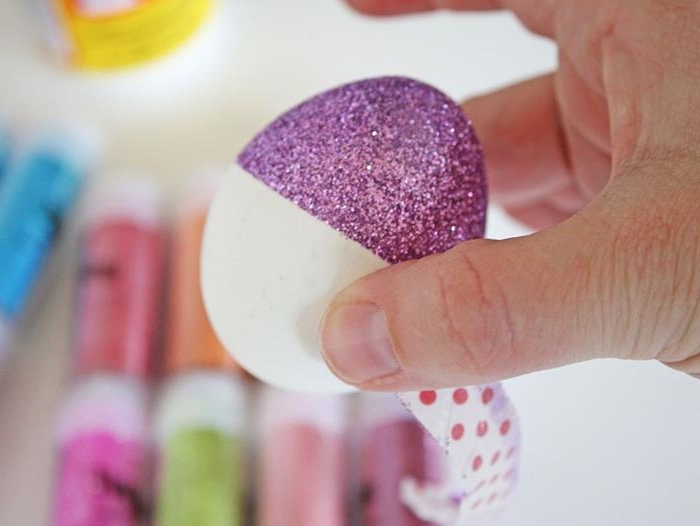 hand holding an egg, half dyed in sparkly purple, half left white, coloring easter eggs, with a half-removed piece of washi tape