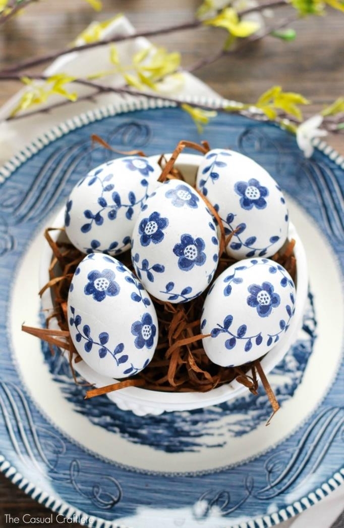 inky blue flower patterns, hand-drawn on white easter eggs, placed in a white bowl, filled with brown easter grass