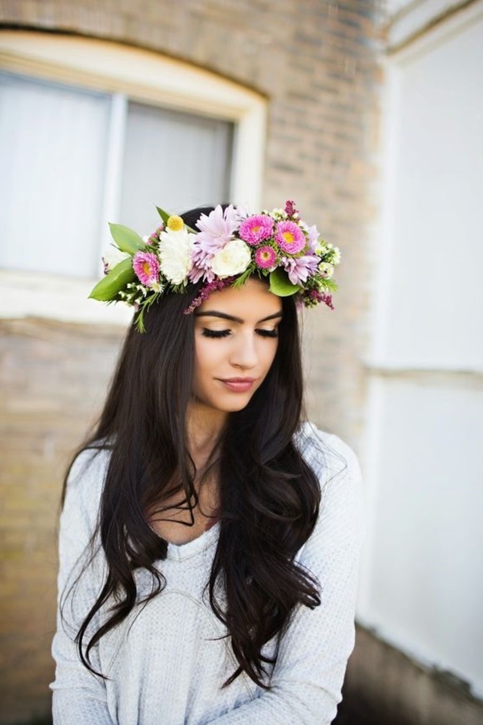 long dark brown, partially curled hair, brunette hairstyles, on a woman in pale grey sweater, wearing large flower crown, with pink white and yellow blossoms